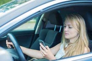 בחורה צעירה מסתכל בטלפון הנייד כשהיא נוהגת