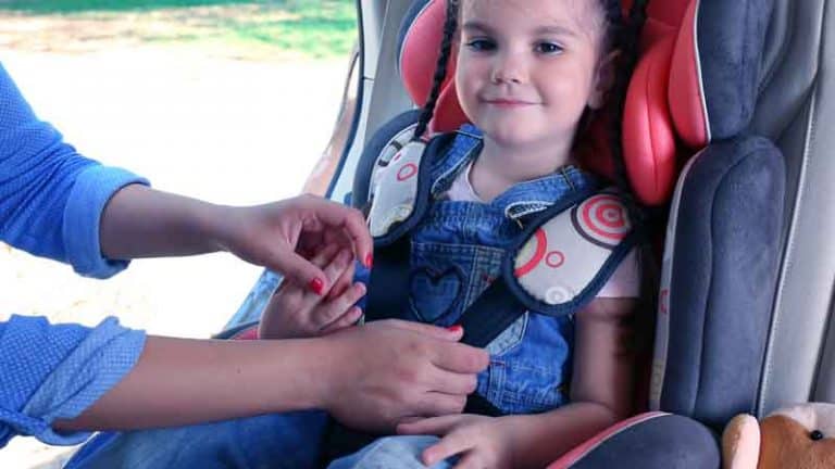 ידיים מתקינות חגורה על מושב בטיחות של ילדה מחייכת במושב האחורי